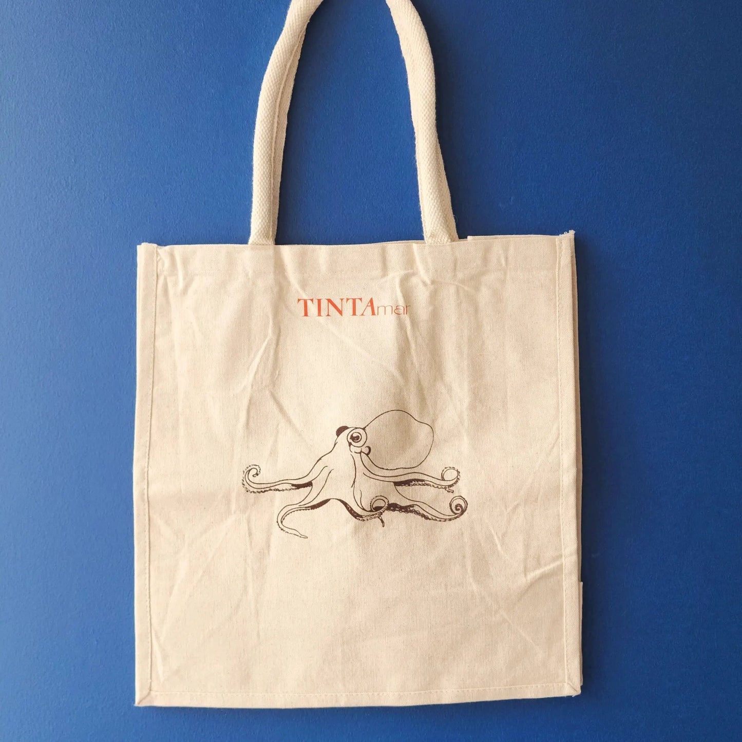 Bolsa de tela TINTAmar color crudo con ilustración de pulpo dibujado a mano sobre fondo azul