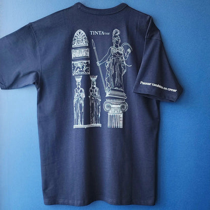 Detalle de polera azul con diseño de Atenea y cariátides, frase “Pausar también es crear” en la manga