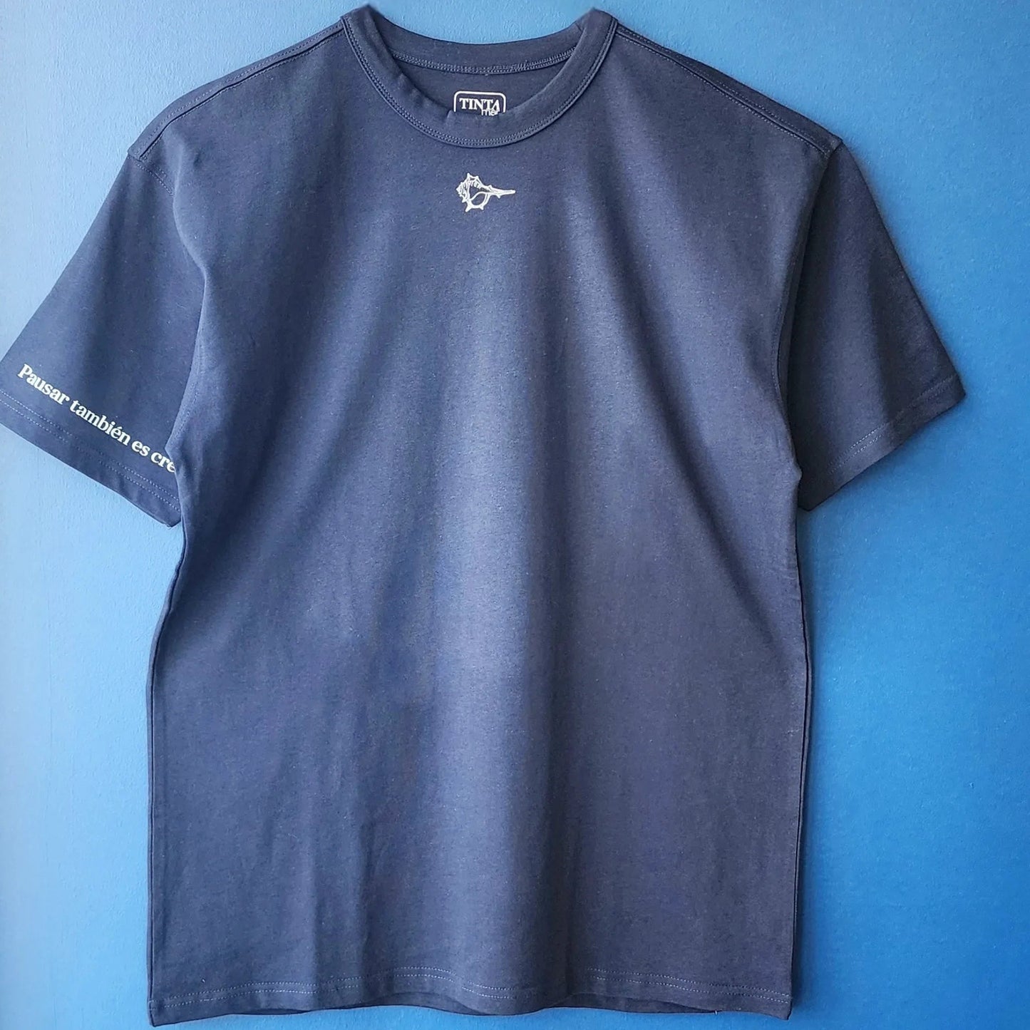 Detalle de polera azul con diseño de Atenea y cariátides, frase “Pausar también es crear” en la manga